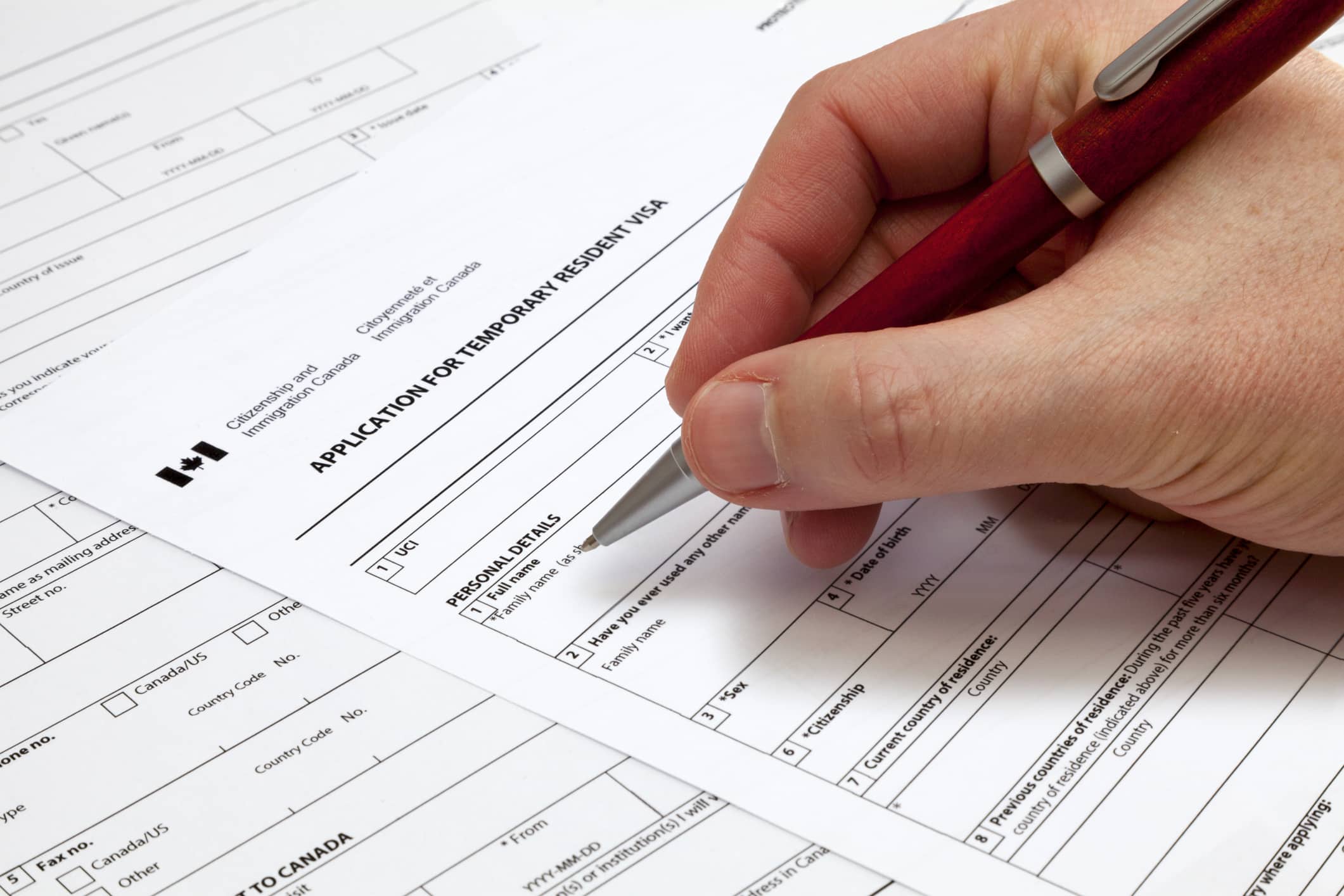 A man holding a ballpoint pen to fill a permanent residence visa application form to Canada.